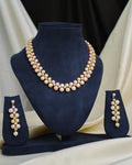 The Royal Mikkimotor Pink CZ Crown Set by Chandrani Pearls, featuring a pearl necklace with a pink CZ crown pendant and matching earrings, is displayed on navy blue velvet stands against a cream and black fabric background.