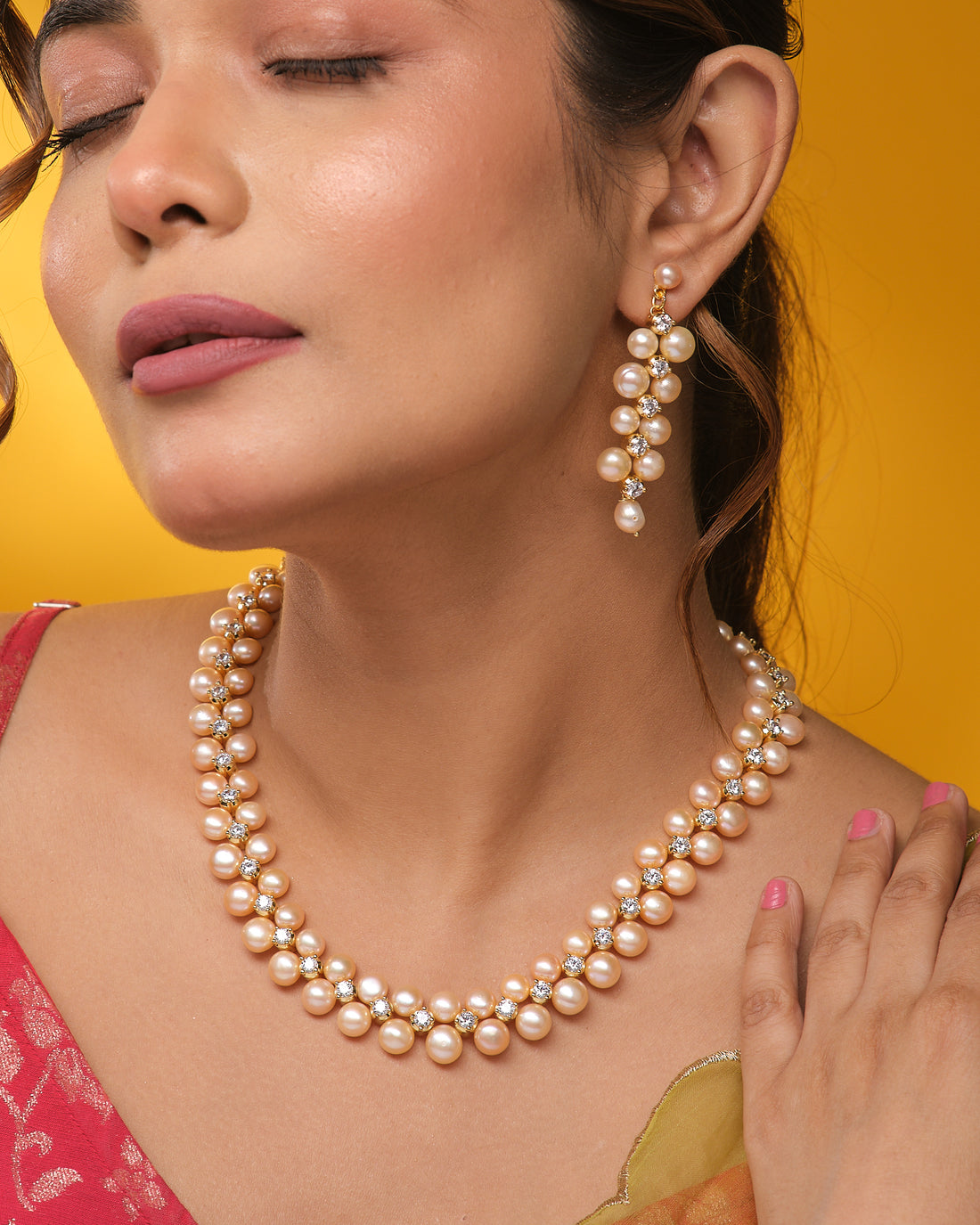 The Royal Mikkimotor Pink CZ Crown Set by Chandrani Pearls, featuring a pearl necklace with a pink CZ crown pendant and matching earrings, is displayed on navy blue velvet stands against a cream and black fabric background.