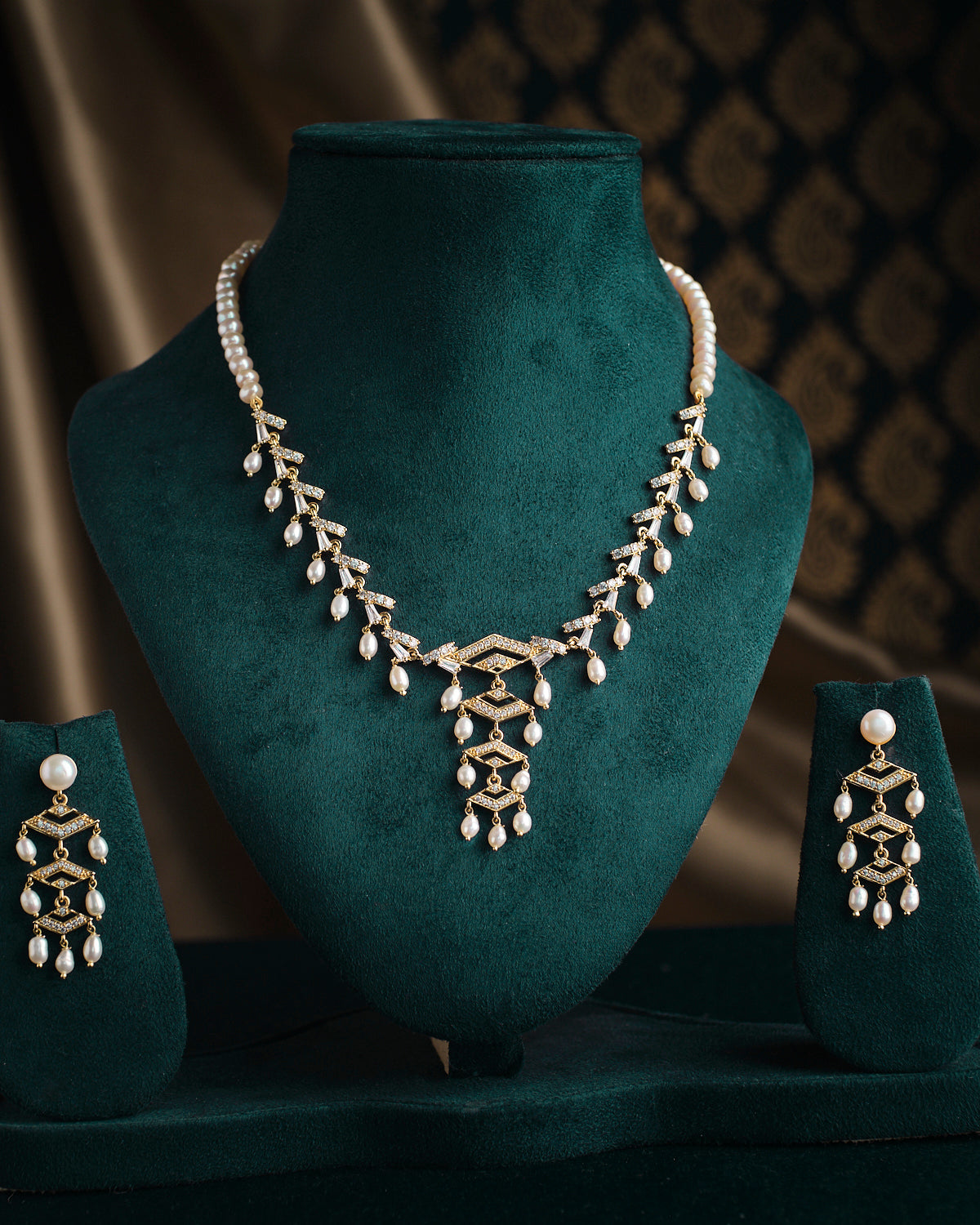 The Jahanara Pearl Necklace Set from Chandrani Pearls is showcased on a dark green velvet stand, complemented by matching earrings on either side.