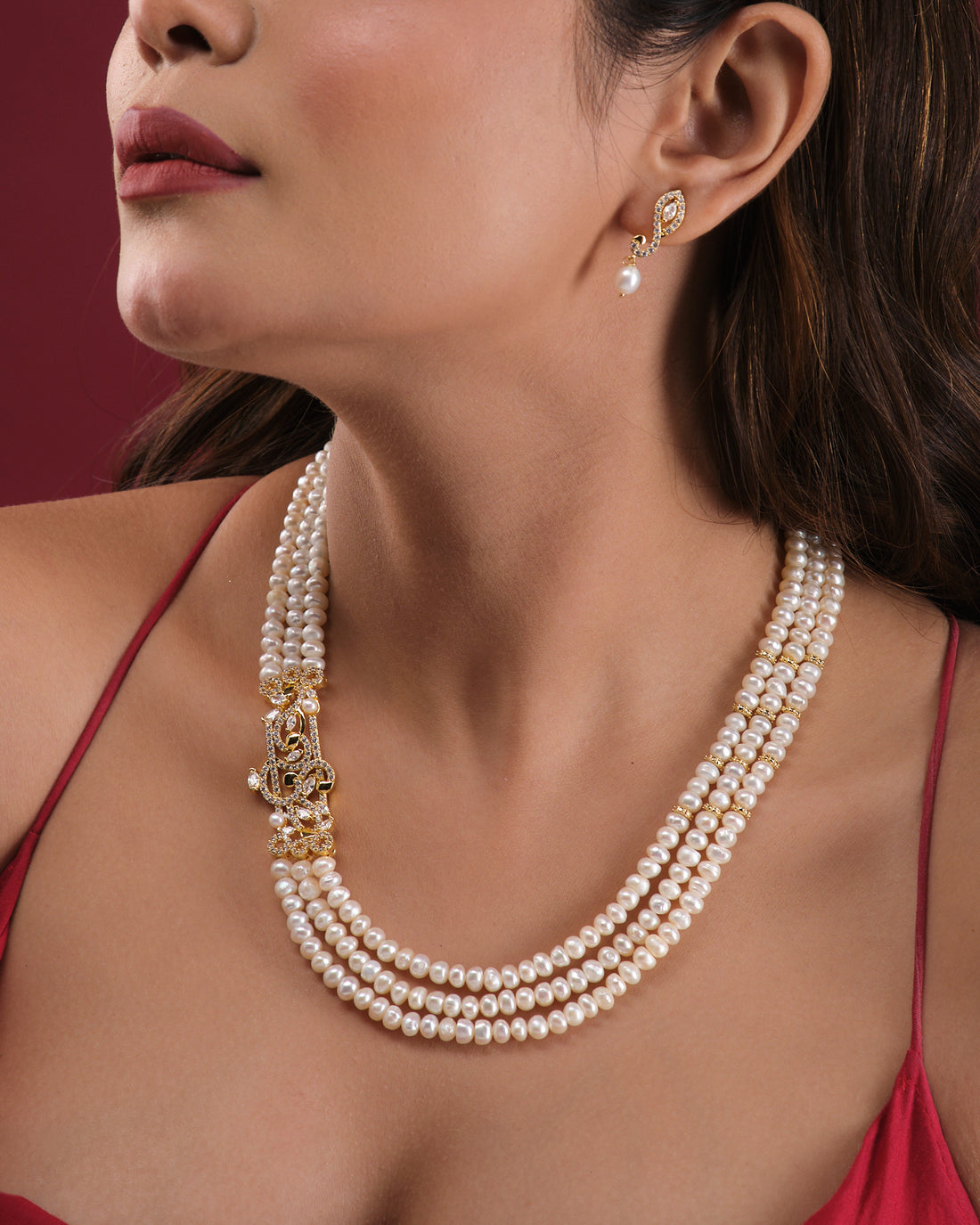 The Ravishing Pearl Necklace Set by Chandrani Pearls India is displayed on a white stand, featuring a gold clasp and matching pearl drop earrings on either side for a timeless, elegant look.