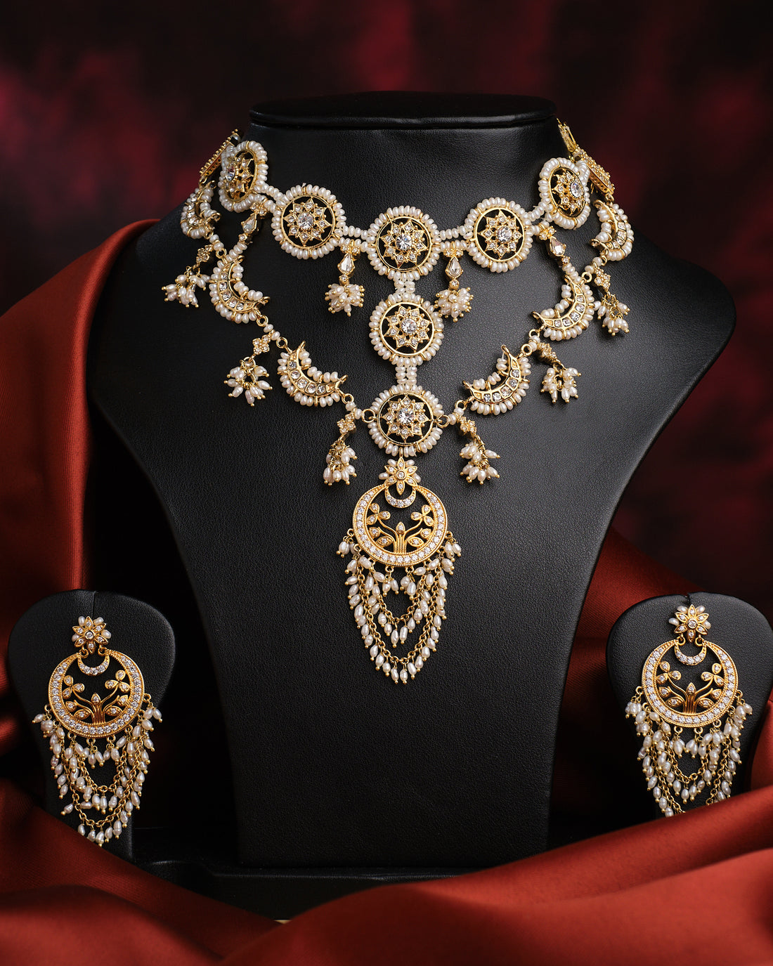 The Padmavati Pearl Necklace Set by Chandrani Pearls features ornate gold and freshwater pearl jewelry, including an intricately designed necklace and matching fine-chained earrings, displayed elegantly on a black stand.