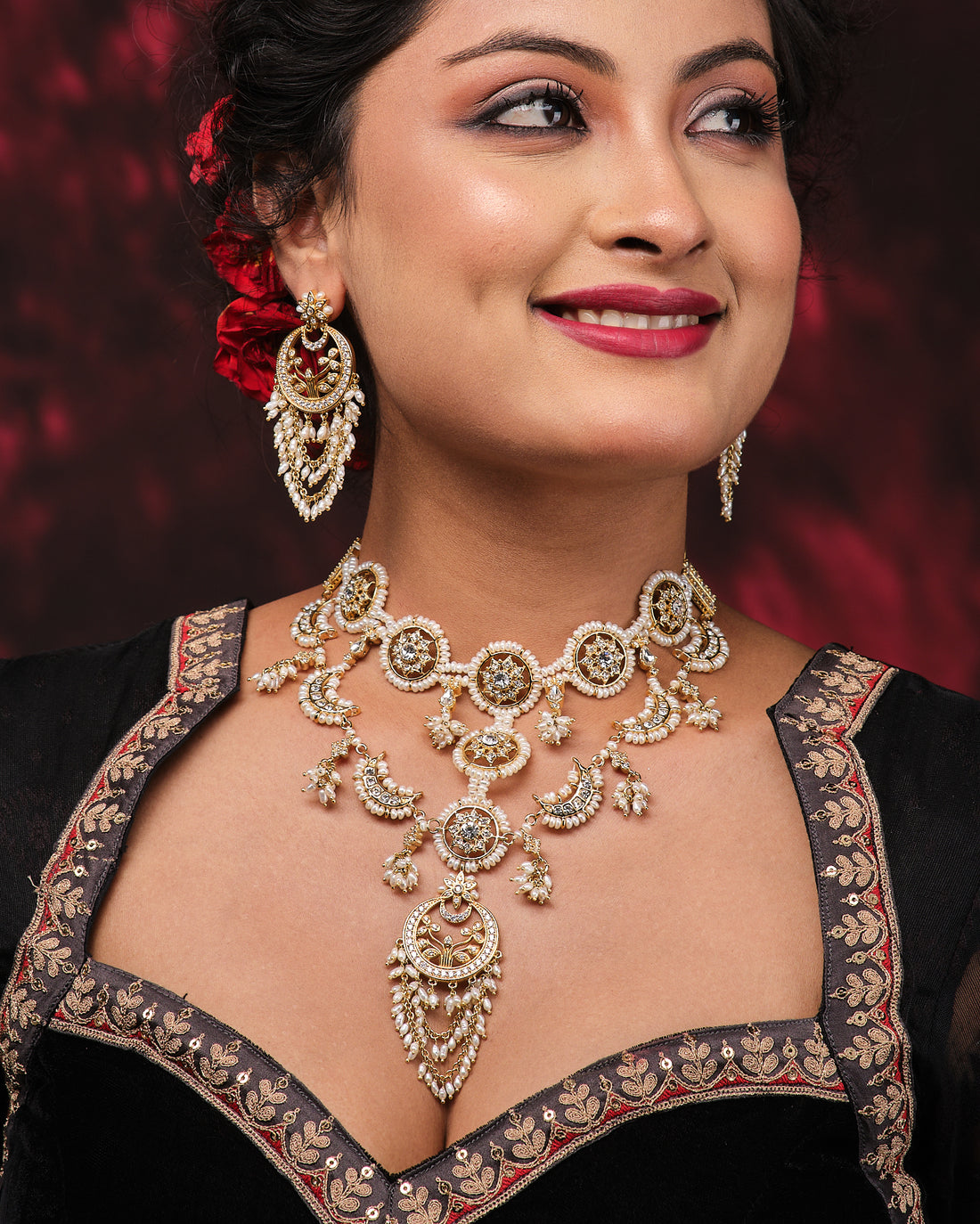 The Padmavati Pearl Necklace Set by Chandrani Pearls features ornate gold and freshwater pearl jewelry, including an intricately designed necklace and matching fine-chained earrings, displayed elegantly on a black stand.