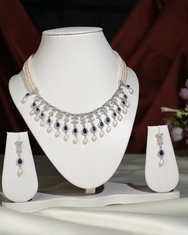 The Trendy Pearl Necklace Set by Chandrani Pearls India exudes elegance and style, featuring a pearl necklace with matching earrings. Displayed on a white jewelry bust, this set stands out beautifully against a blurred background.