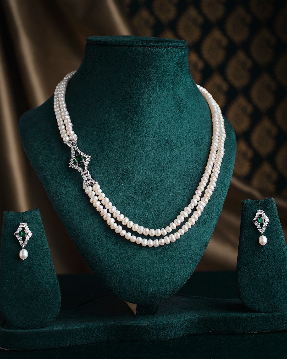 Amoha- The Mesmerising Twilight Pearl Necklace Set by Chandrani Pearls is showcased with a decorative clasp on a green stand, complemented by matching earrings.