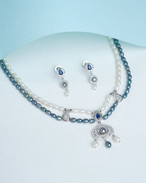 Chandrani Pearls’ Dainty pearl necklace with matching earrings adds an elegant finish, shown here on a white surface with blue accents and a curved blue sheet for a classic, refined look.