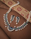 The Luxe Pearl Beautiful Necklace Set by Chandrani Pearls with matching earrings is displayed on brown fabric beside a gold and red embroidered textile.