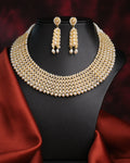 The Suvarnachandra-Golden Moon Royal Pearl Necklace Set by Chandrani Pearls, featuring gold and pearl with crystal accents and matching earrings, is displayed on a black jewelry stand draped with satin red fabric.