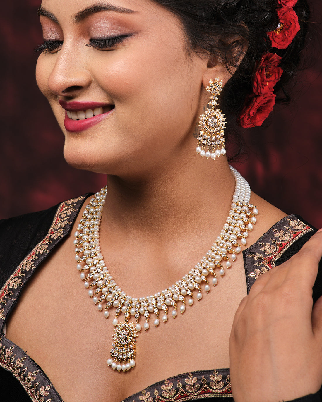 The Suryaprabha-Luxe Heritage Pearl Necklace Set by Chandrani Pearls, displayed with matching earrings on a black bust against a dark backdrop and red fabric accent, exudes timeless elegance.