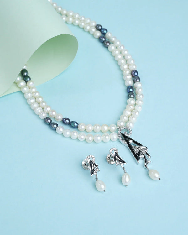 The Beautifully handcrafted pearl necklace with delicate matching hangs by Chandrani Pearls is elegantly displayed on a blue surface, featuring black and white beads and matching earrings with a rolled sheet as decoration.