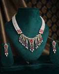 The Anvesha Necklace Set by Chandrani Pearls India, featuring a pearl and gemstone necklace with matching earrings, is showcased on a dark green stand.