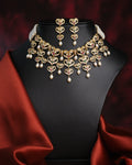The Dazzling Pearl Necklace Set by Chandrani Pearls features a gold and gemstone necklace with matching earrings, accented with pearls and red fabric on a black bust—ideal for formal occasions.