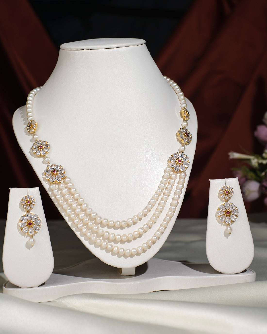 A white display stand features the Flory Double Side Necklace Set by Chandrani Pearls India—a sophisticated three-layer pearl necklace with gold and stone accents, paired with matching pearl drop earrings.