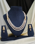 The Chandrani Pearls Layered CZ Necklace & Earring Set is showcased on navy blue velvet stands, creating an elegant and dramatic effect against a draped fabric background.