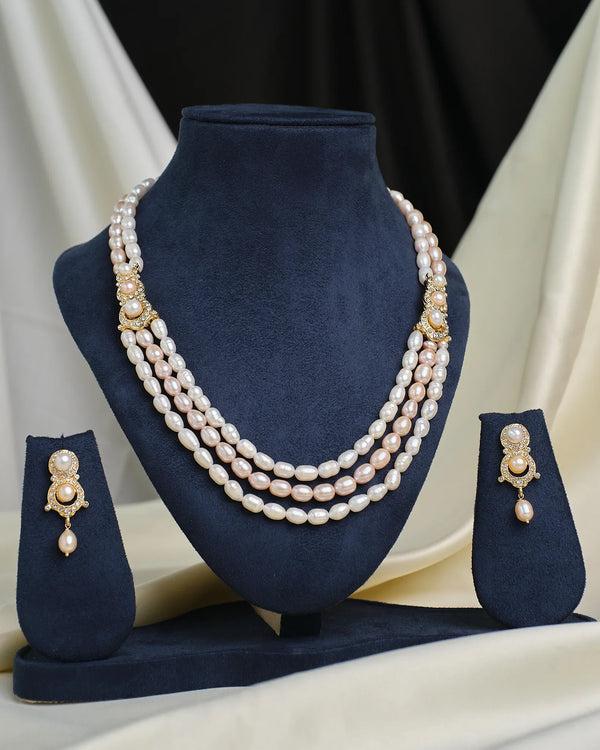 The Chandrani Pearls Layered CZ Necklace & Earring Set is showcased on navy blue velvet stands, creating an elegant and dramatic effect against a draped fabric background.