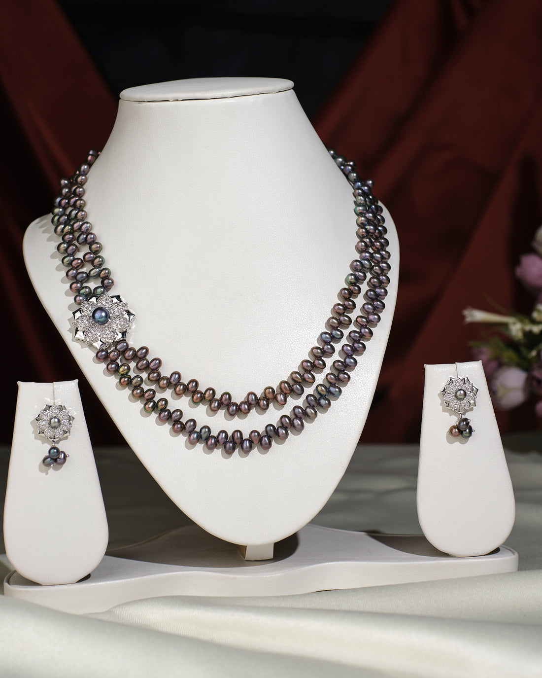 The Florial Side Pearl Black Set by Chandrani Pearls India features a stylish two-strand pearl necklace with a silver clasp and matching earrings, elegantly displayed on a white stand—an ideal complement to any outfit.