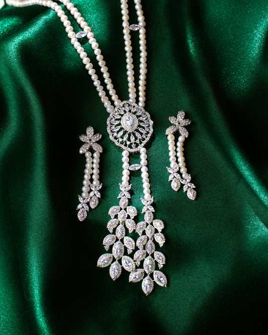 The Deepa's Evening Glamour Necklace Set by Chandrani Pearls, adorned with pearls and diamonds, is showcased with matching earrings on a green velvet stand against a patterned backdrop, embodying the elegance of Glamour Jewelry for any sophisticated occasion.