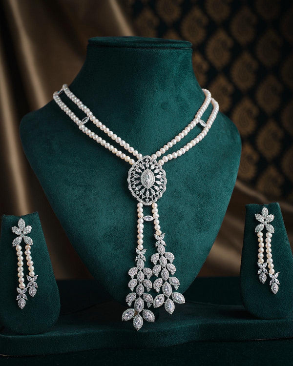 The Deepa's Evening Glamour Necklace Set by Chandrani Pearls, adorned with pearls and diamonds, is showcased with matching earrings on a green velvet stand against a patterned backdrop, embodying the elegance of Glamour Jewelry for any sophisticated occasion.