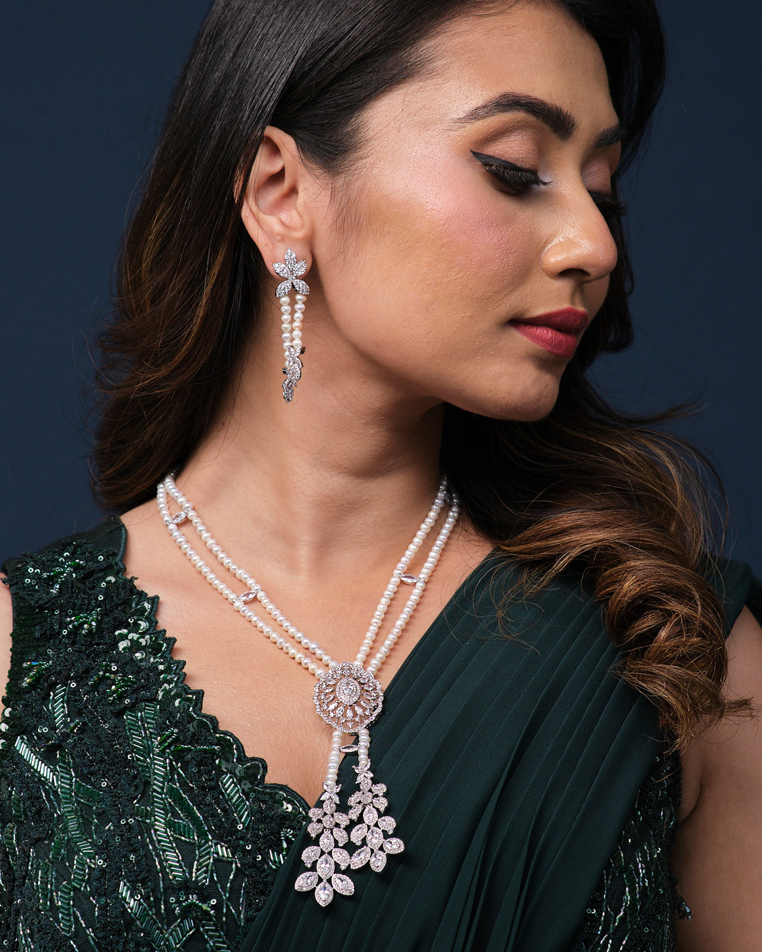 The Deepa's Evening Glamour Necklace Set by Chandrani Pearls, adorned with pearls and diamonds, is showcased with matching earrings on a green velvet stand against a patterned backdrop, embodying the elegance of Glamour Jewelry for any sophisticated occasion.