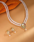 The Celina CZ Pearl Set by Chandrani Pearls—featuring a refined double-strand pearl necklace with a gold and gemstone pendant plus matching pearl and gold earrings—radiates timeless brilliance on a tan background.