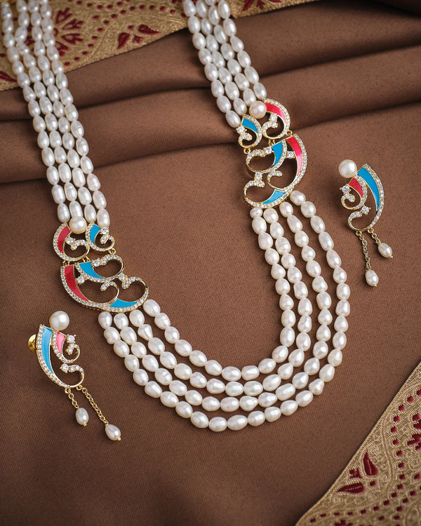 The Graceful Queen Pearl CZ Necklace Set by Chandrani Pearls features three strands with gold, red, and blue accents, plus matching earrings, displayed on brown fabric with a patterned border—exuding regal grace.