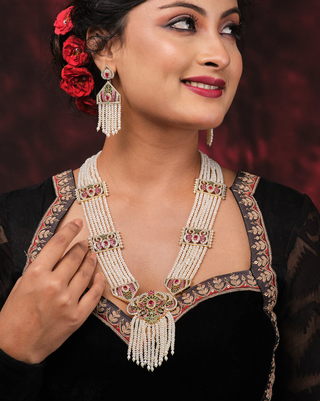 The Sindurya-Scarlet Ray's Lahari Sitahar Set by Chandrani Pearls features a multi-strand pearl necklace with matching earrings, gold, green, and pink accents, vintage-style clasp—displayed on black against red fabric—a timeless heirloom piece.