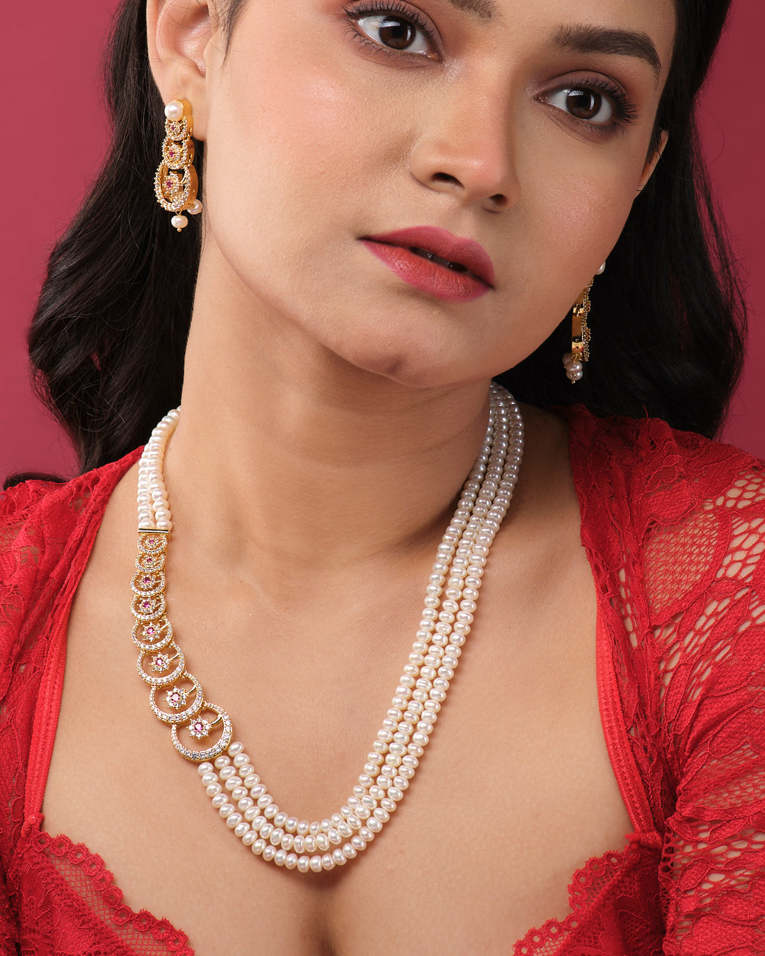 The Ravishing Pearl Necklace Set by Chandrani Pearls India, with a gold and pink accent, is displayed on a white stand alongside matching earrings on smaller stands—ideal for both formal and casual occasions.
