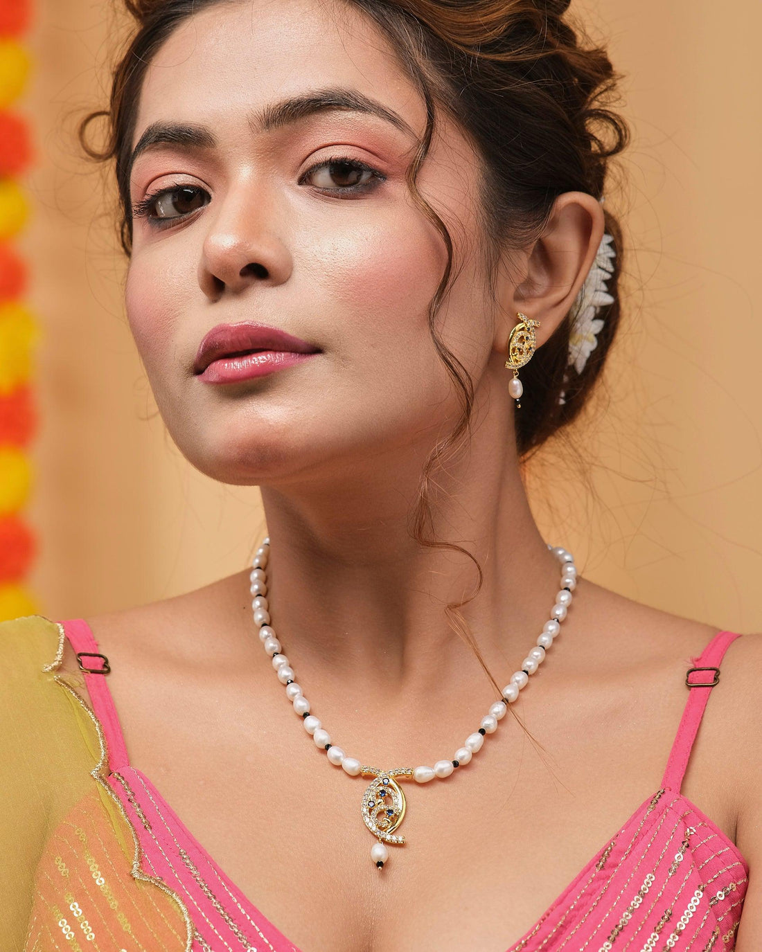 The Adorable Aura Pearl Necklace Set by Chandrani Pearls, featuring a necklace with a decorative pendant elegantly displayed on a velvet stand, is complemented by matching earrings presented on a red box, all set against a softly lit background.