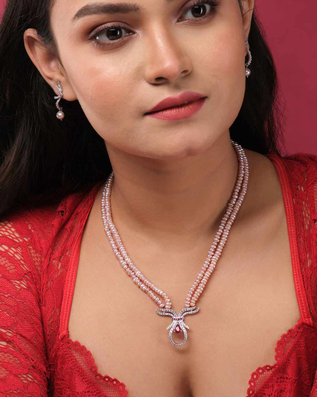 The Beautiful Pearl Necklace Set by Chandrani Pearls India features a pink beaded necklace with pearls and a central pendant, plus matching earrings—ideal for both casual and formal wear. Displayed elegantly on stands against a neutral background.