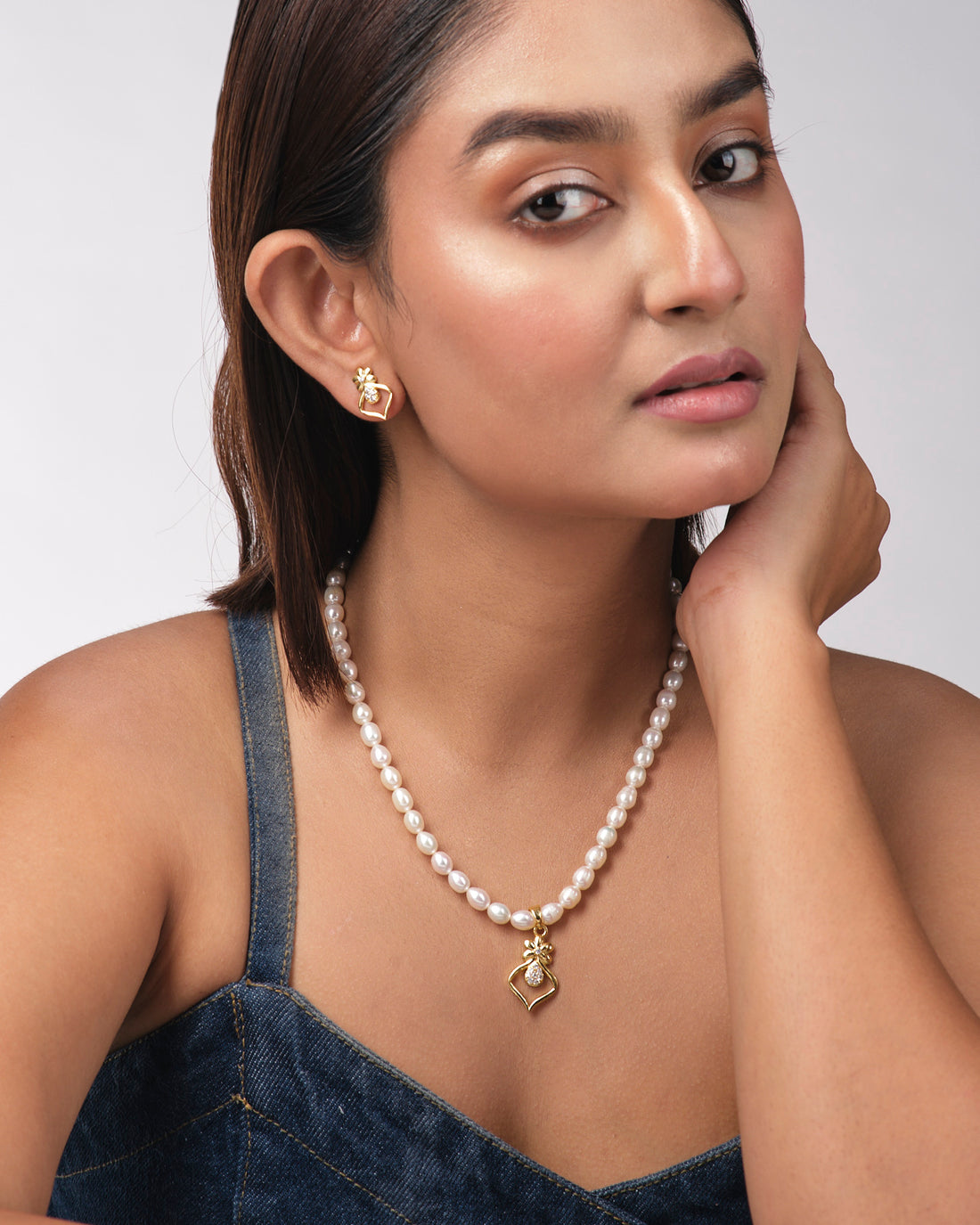 The Pretty Pearl Necklace Sets by Chandrani Pearls India, featuring a gold and diamond pendant, are displayed with matching earrings on a light yellow background.