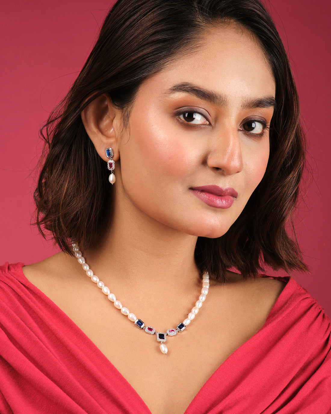 The Camelia CZ Stone 1 Line Necklace Set by Chandrani Pearls India is displayed on a stand, featuring a pearl necklace with blue and pink stones, drop pendant, and matching earrings—an elegant addition to any wardrobe.