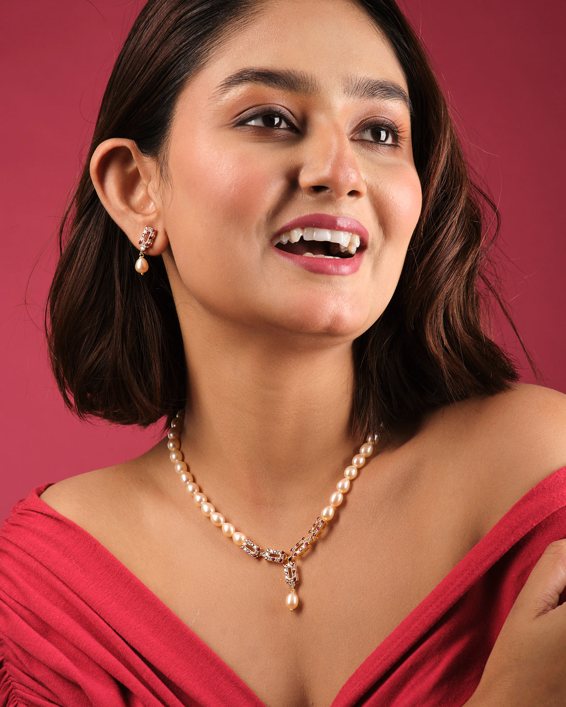 The Yamie CZ Stone 1 Line Necklace Set by Chandrani Pearls India features a pearl pendant necklace and matching drop earrings on display stands, bringing timeless elegance to any wardrobe with a floral backdrop.