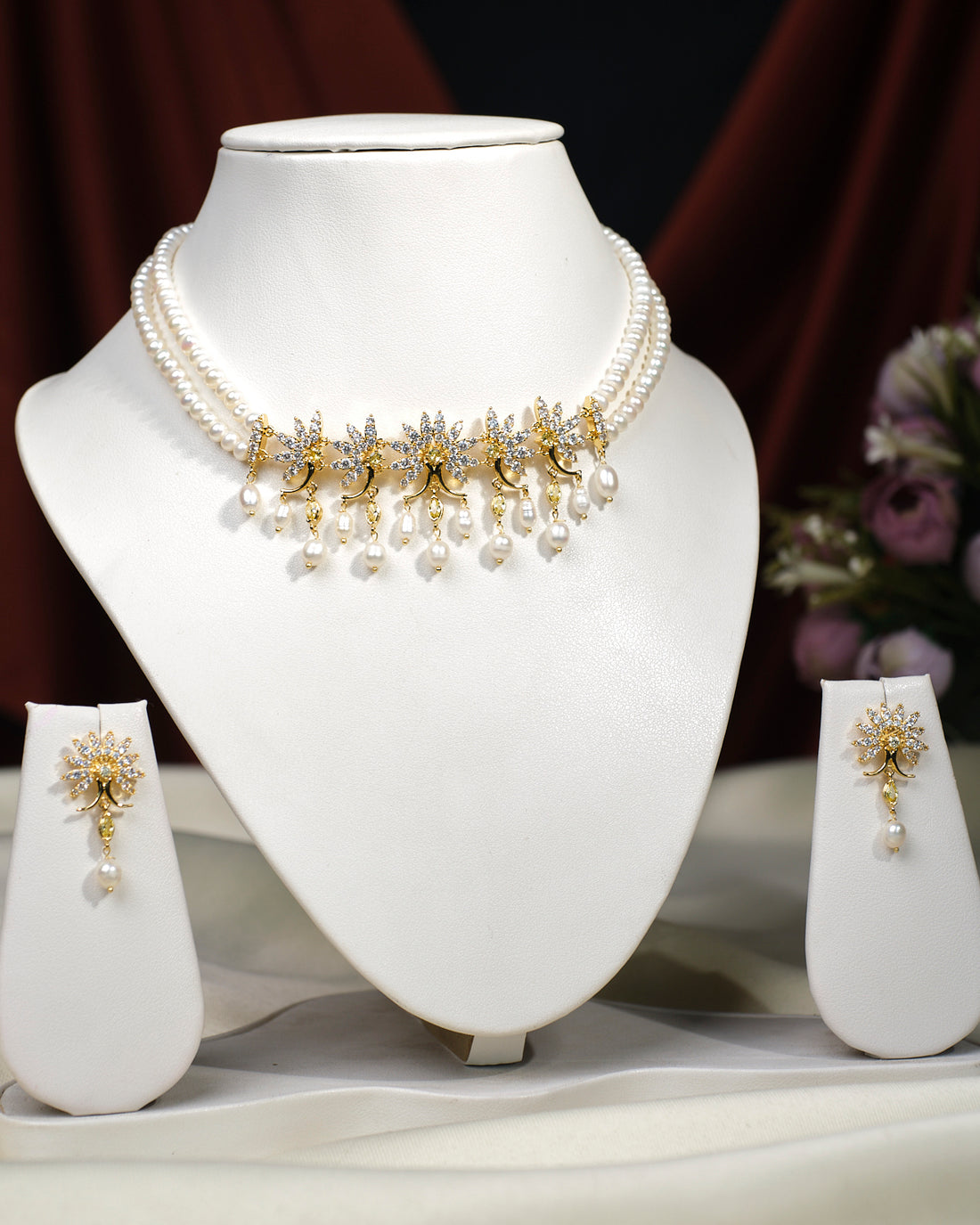 The Crystal Crest Necklace Set by Chandrani Pearls India features a pearl necklace with gold and diamond floral motifs and dangling pearls, displayed on a white bust with matching earrings—perfect for elegant, fashion-forward looks.