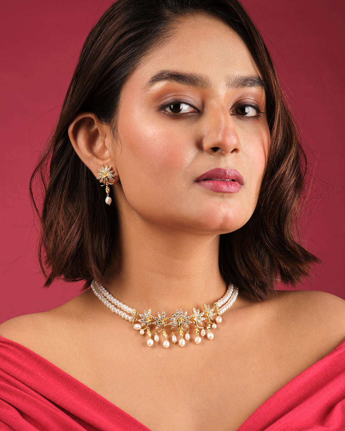The Crystal Crest Necklace Set by Chandrani Pearls India features a pearl necklace with gold and diamond floral motifs and dangling pearls, displayed on a white bust with matching earrings—perfect for elegant, fashion-forward looks.
