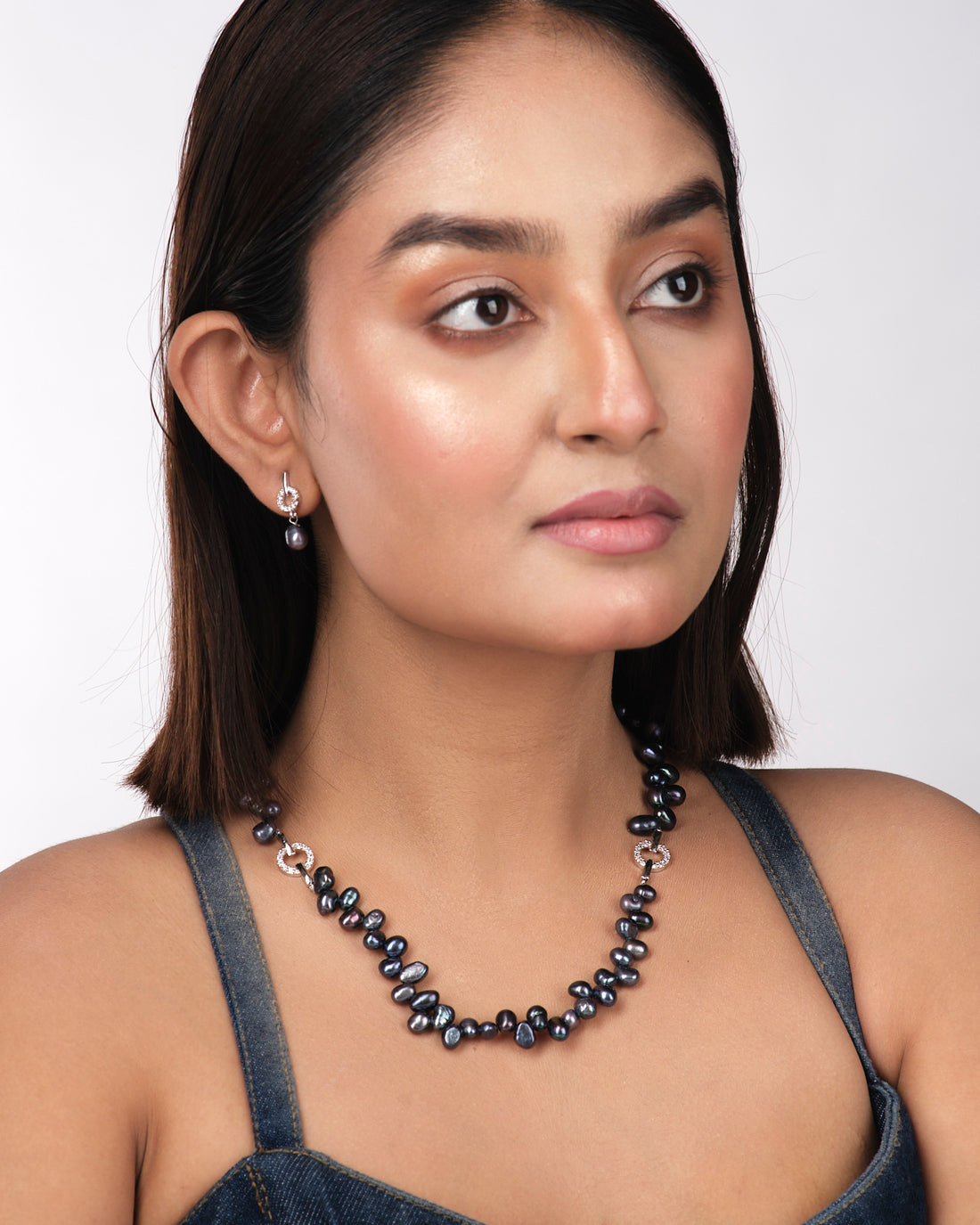The Trendy Pearl Necklace Set by Chandrani Pearls India features dark pearls and small circular diamond accents, exuding timeless brilliance against a light yellow background.