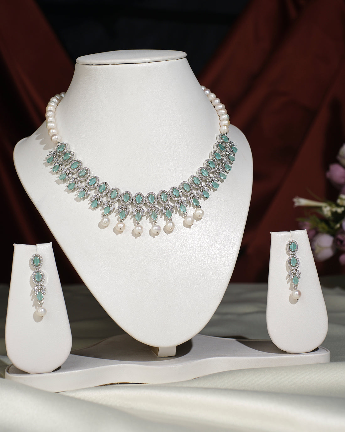 The Gorgeous Olive CZ Pearl Necklace Set by Chandrani Pearls India, featuring a necklace with matching earrings, exudes elegance as it is displayed on a white jewelry stand against a dark backdrop.