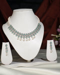 The Gorgeous Olive CZ Pearl Necklace Set by Chandrani Pearls India, featuring a necklace with matching earrings, exudes elegance as it is displayed on a white jewelry stand against a dark backdrop.