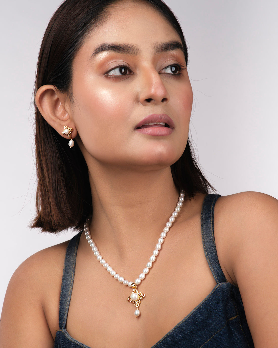 The Regal Pearl Necklace Sets by Chandrani Pearls India, featuring gold earrings with pearl and crystal accents, are showcased on a light yellow surface—an elegant choice for the modern woman.
