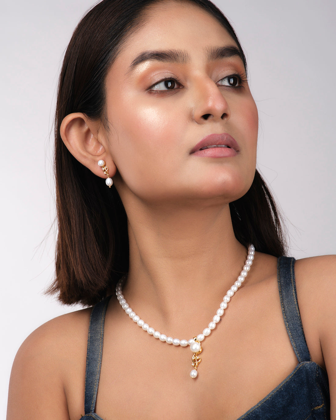 Chandrani Pearls India's Elegant Pearl Necklace Sets, featuring a gold and pearl pendant with matching drop earrings, are showcased on a pale yellow background—a sophisticated choice for today's modern woman.