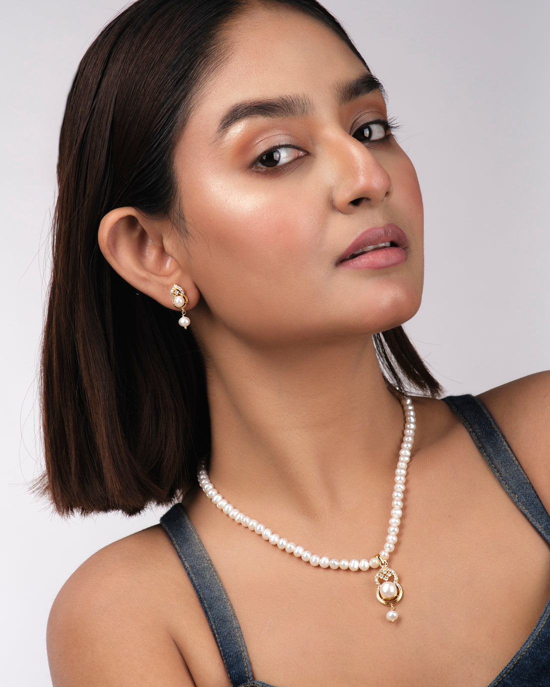 The Pretty Pearl Necklace Sets by Chandrani Pearls India, featuring a necklace and matching earrings with luminous pearls and clear stones, are displayed on a pale yellow background to accentuate their elegance.