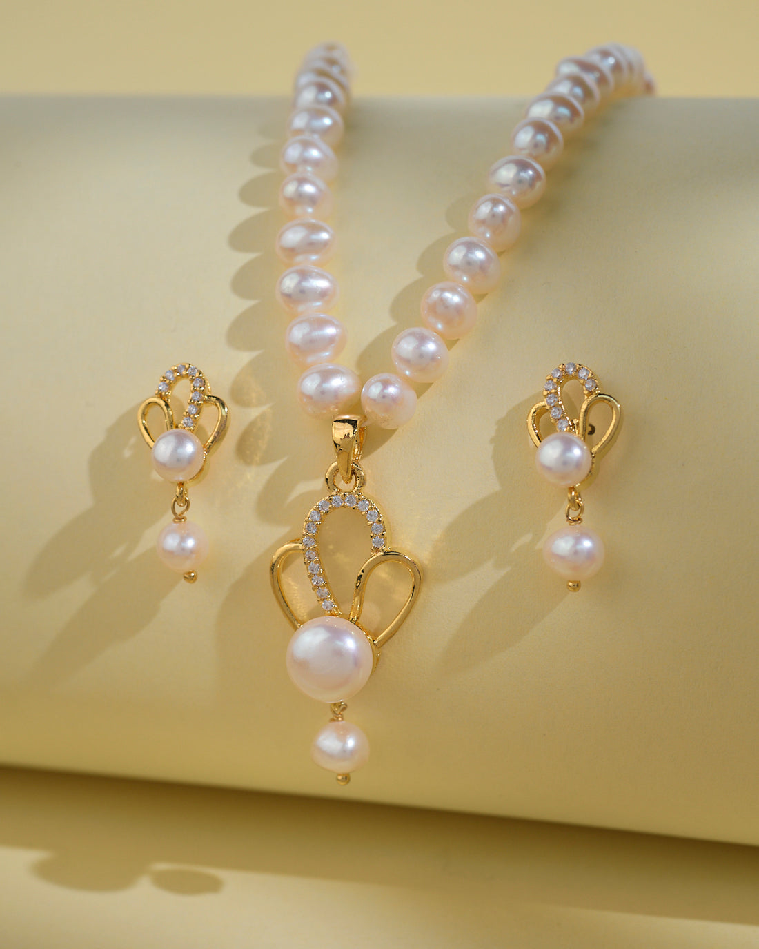 The Elegant Pearl Necklace Sets by Chandrani Pearls India, featuring a necklace and matching earrings, are displayed on a light beige background to highlight the pearls' natural beauty.