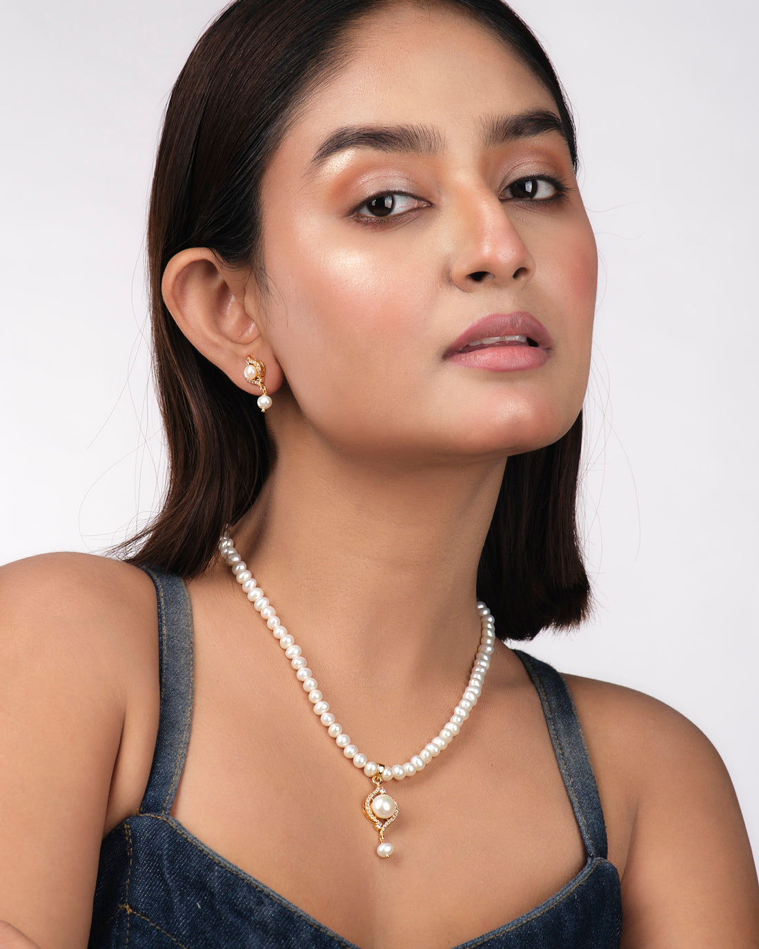 The Simple Pearl Necklace Sets by Chandrani Pearls India include a pearl necklace with gold and diamond accents and matching earrings, elegantly displayed on a pale yellow surface to enhance their natural beauty.