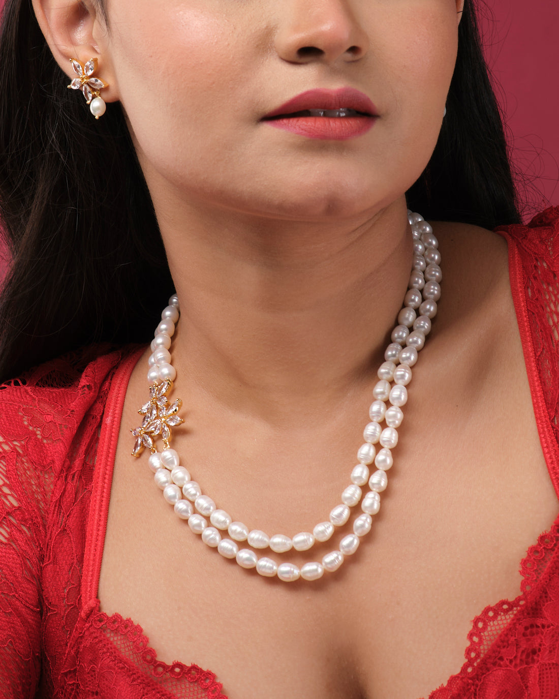 The Floral Pearl Necklace Set by Chandrani Pearls India features a double-stranded pearl necklace with a gold floral brooch and matching pearl and gold earrings, all displayed elegantly on a white stand.