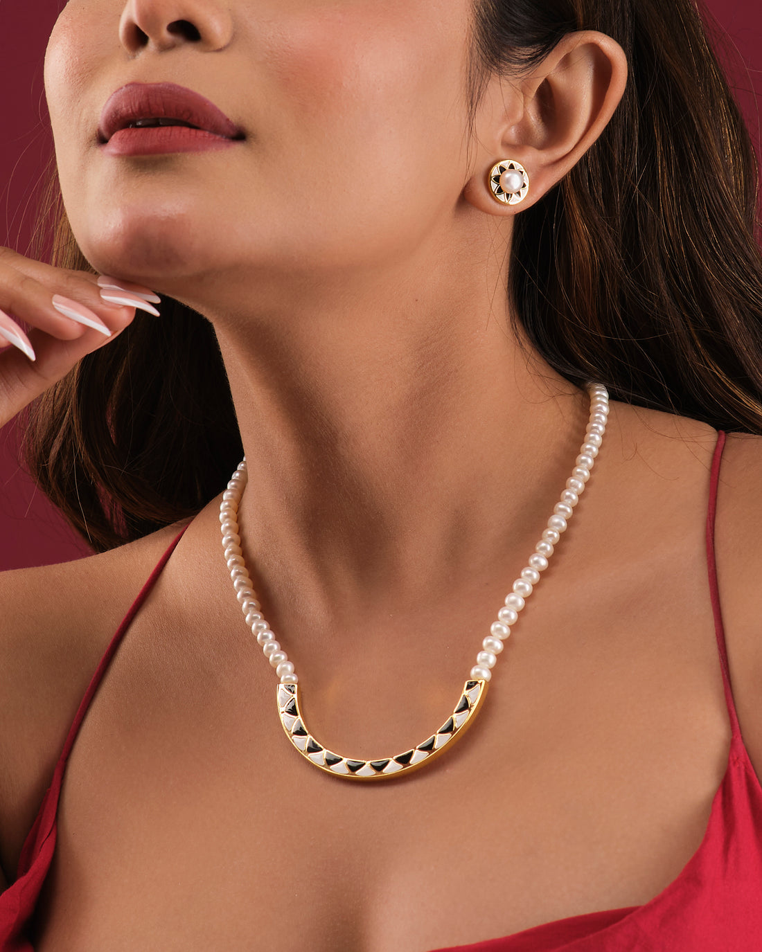 The Elegant Pearl Necklace Set by Chandrani Pearls India features a black and gold pendant on a pearl necklace displayed on a white stand, paired with matching round earrings.
