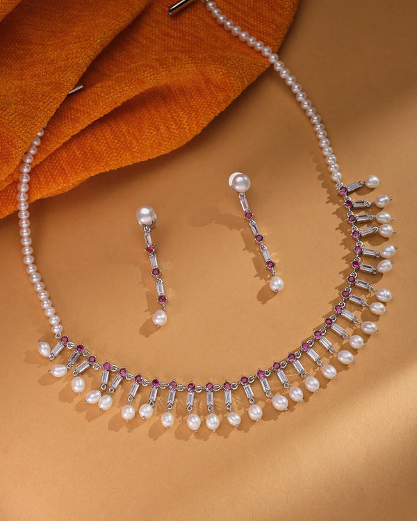 The Iridescent Real Pearl Jewelry Set Dreamy & Dazzling by Chandrani Pearls features pearls with purple gemstones and matching earrings—showcasing natural sheen on a brown surface with orange fabric, perfect statement jewelry for any occasion.