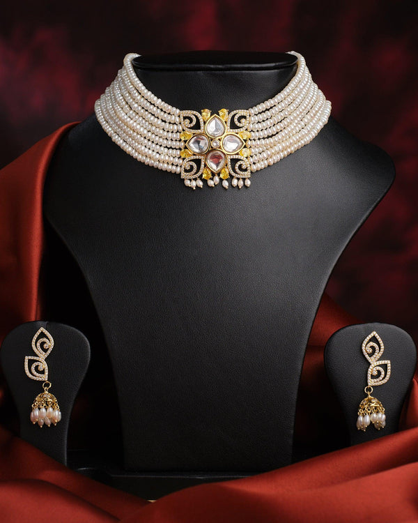 The Viveka Pearl Necklace Set by Chandrani Pearls features a vintage layered pearl necklace with a gold and gemstone floral centerpiece on a black stand, paired with matching gold and pearl earrings.