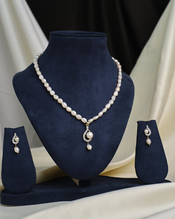 The Chandrani Pearls Layered CZ Necklace & Earring Set, featuring shimmering stones, is elegantly displayed on a dark blue velvet stand with a draped cream and black fabric background.