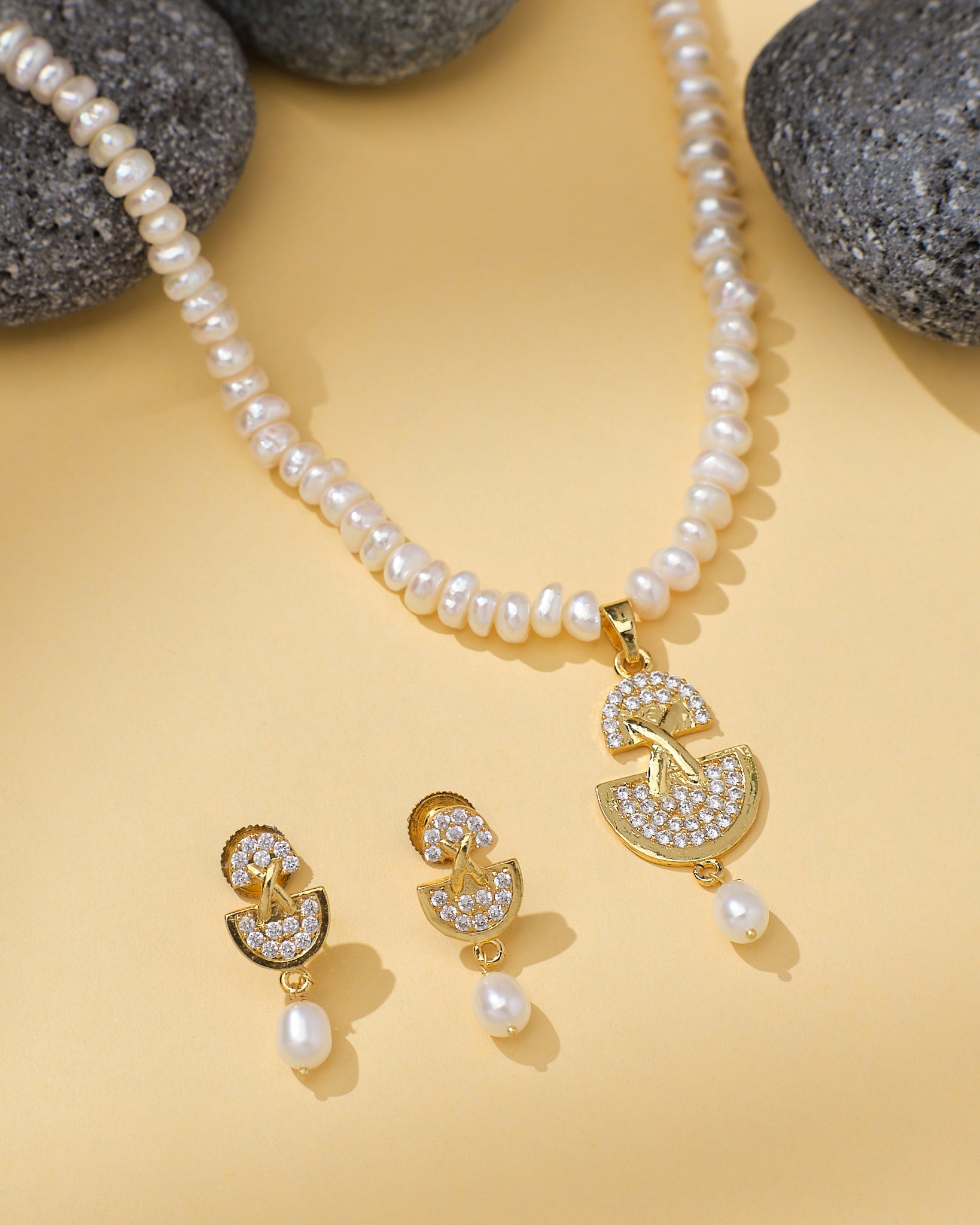 The Modern Necklace Pearl Set by Chandrani Pearls features a gold and CZ crystal pendant with matching earrings, beautifully displayed on yellow with black stones—ideal for the stylish woman.