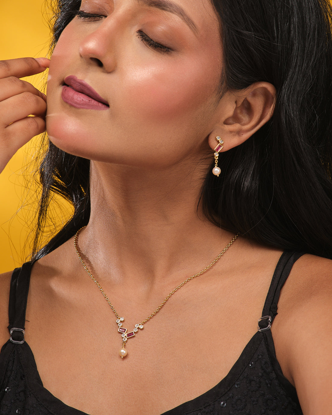 The Pure Elegance Pretty Set by Chandrani Pearls features a gold necklace and matching earrings with geometric designs, red accents, CZ stones, and pearl drops—ideal for formal occasions or gifting—shown on beige with orange textured fabric.
