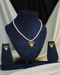 The Leaf Design CZ Jewelry Set by Chandrani Pearls features a necklace with a gold and pearl leaf-shaped pendant on a navy stand, complemented by matching pearl and gold earrings displayed on smaller stands.