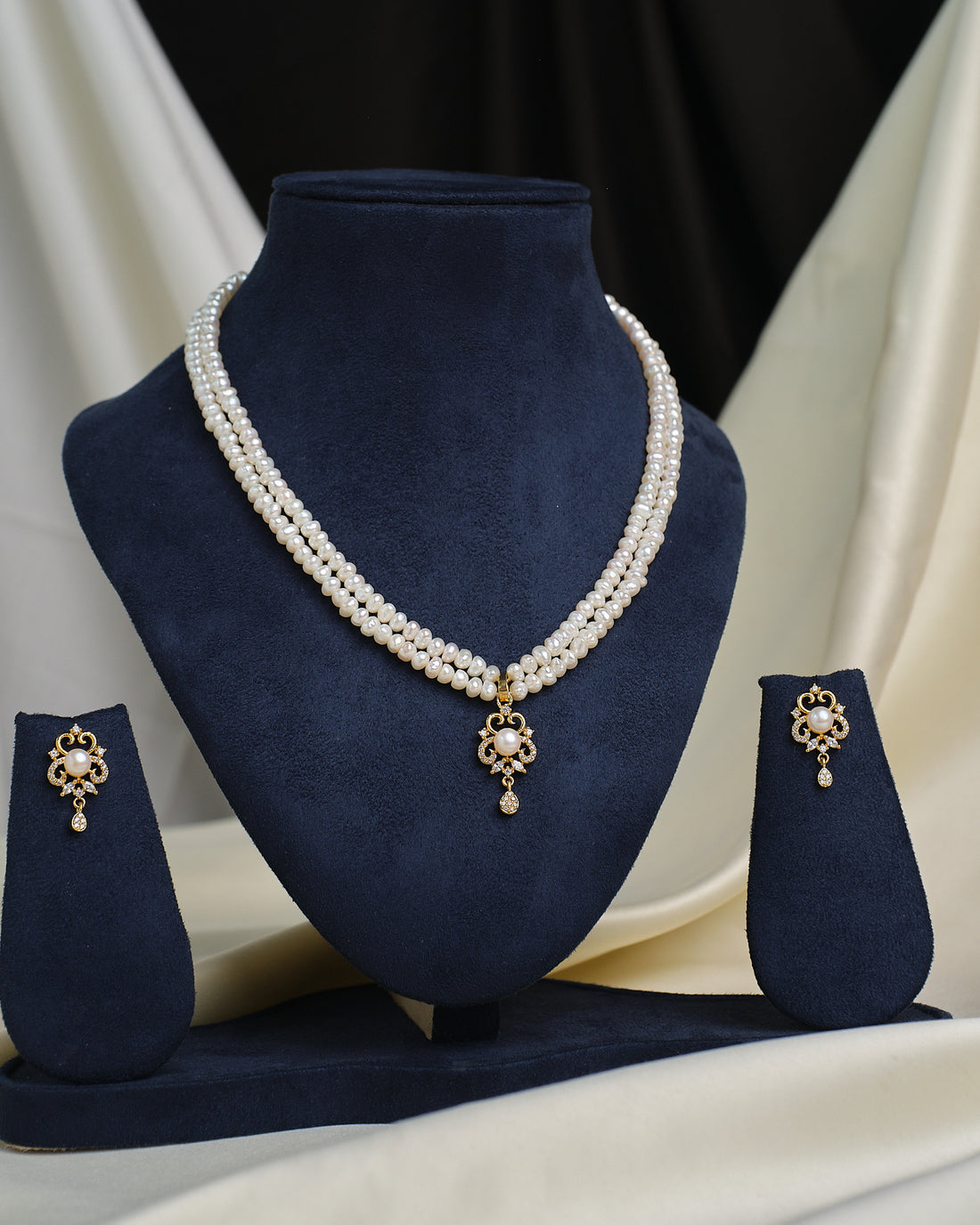 The Elegant round-cut CZ pendant with matching earrings by Chandrani Pearls, displayed on a navy stand, offers timeless style—designed to add everyday sparkle to your look.